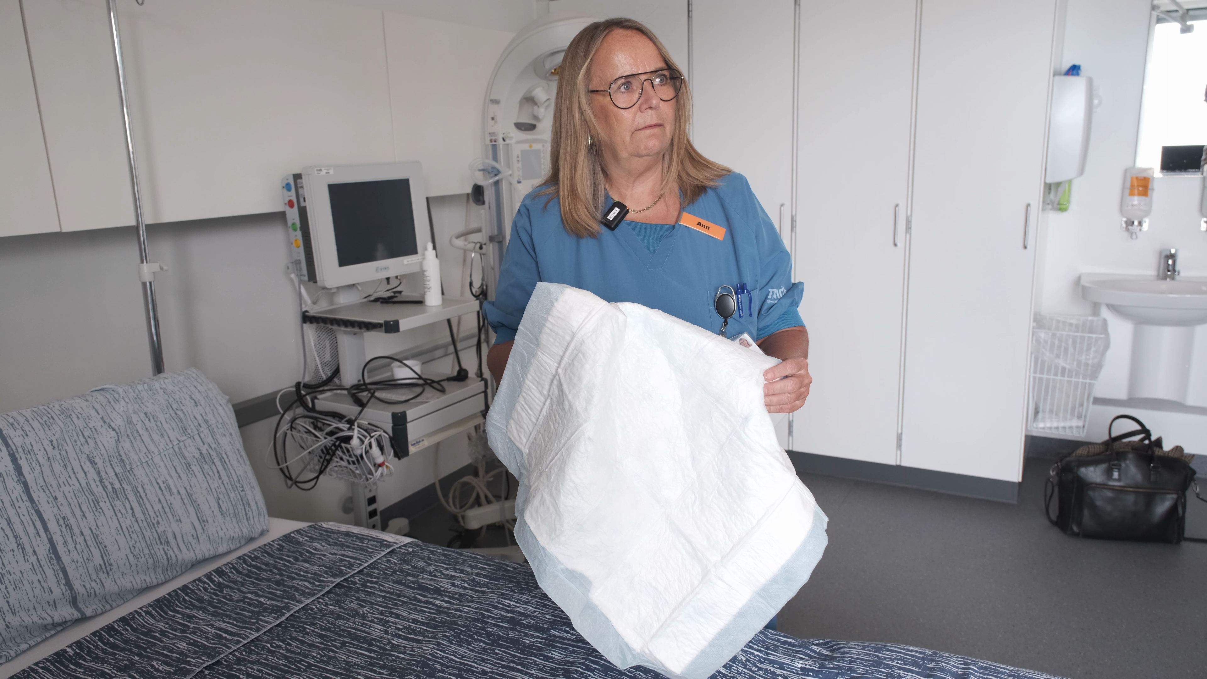 Chefjordemoder Ann Fogsgaard står ved siden af en hospitalsseng med et flergangsunderlag i hænderne.