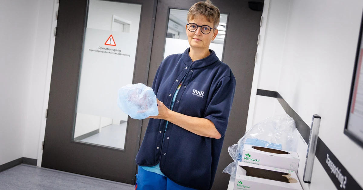 Serviceassistent står på hospitalsgang iført flergangsvarmejakken.