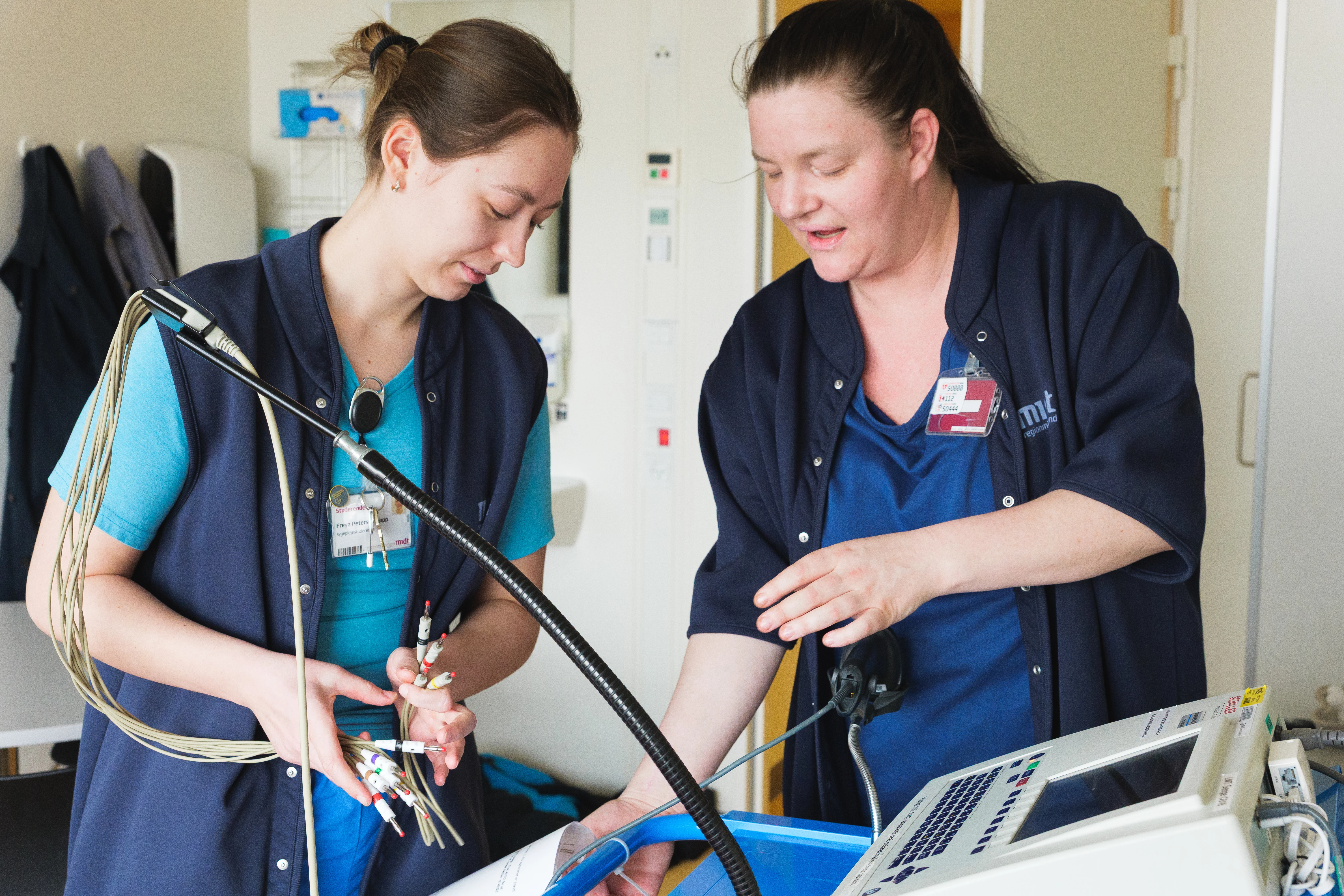 To sygeplejersker samarbejder ved en monitor på en hospitalsstue.