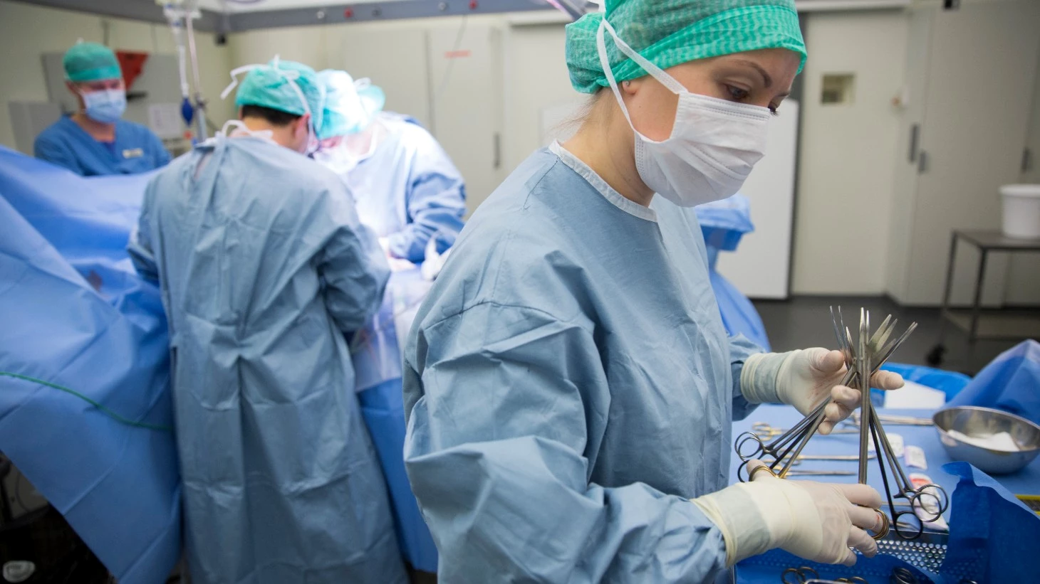 4 klinikere står i fuld operationsudstyr omgivet af store mængder afdækning og engangsudstyr.