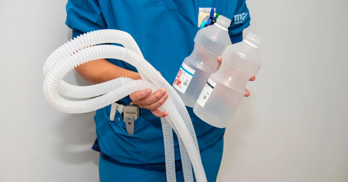Sygeplejerske i blå uniform står med plastikaffald i hænderne.